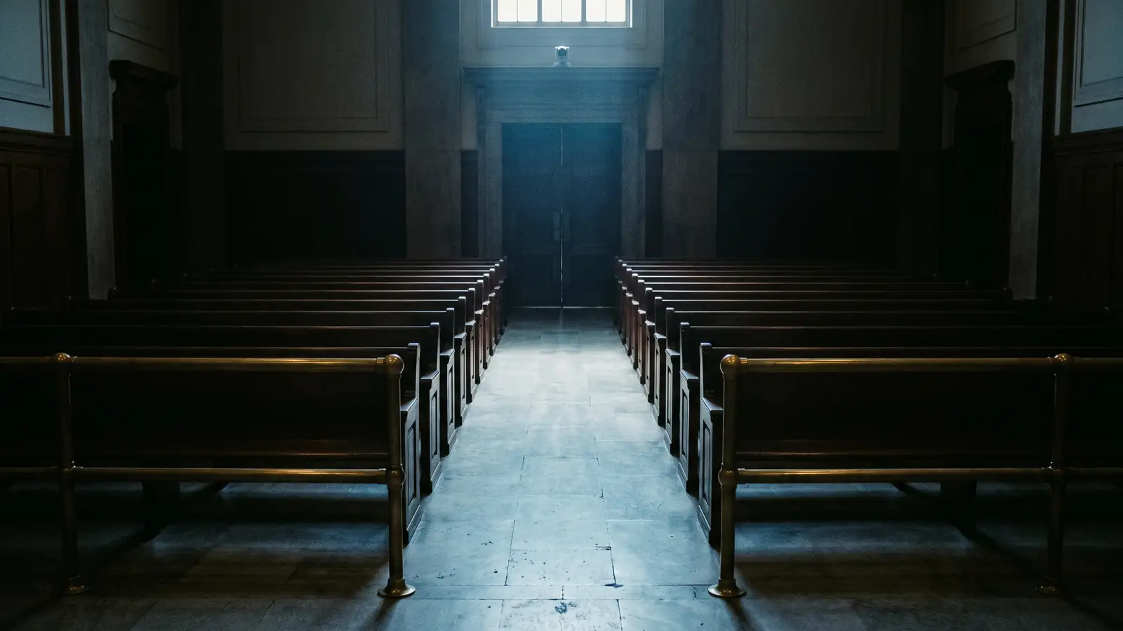 An empty courtroom gallery at night, benches receding into shadow.